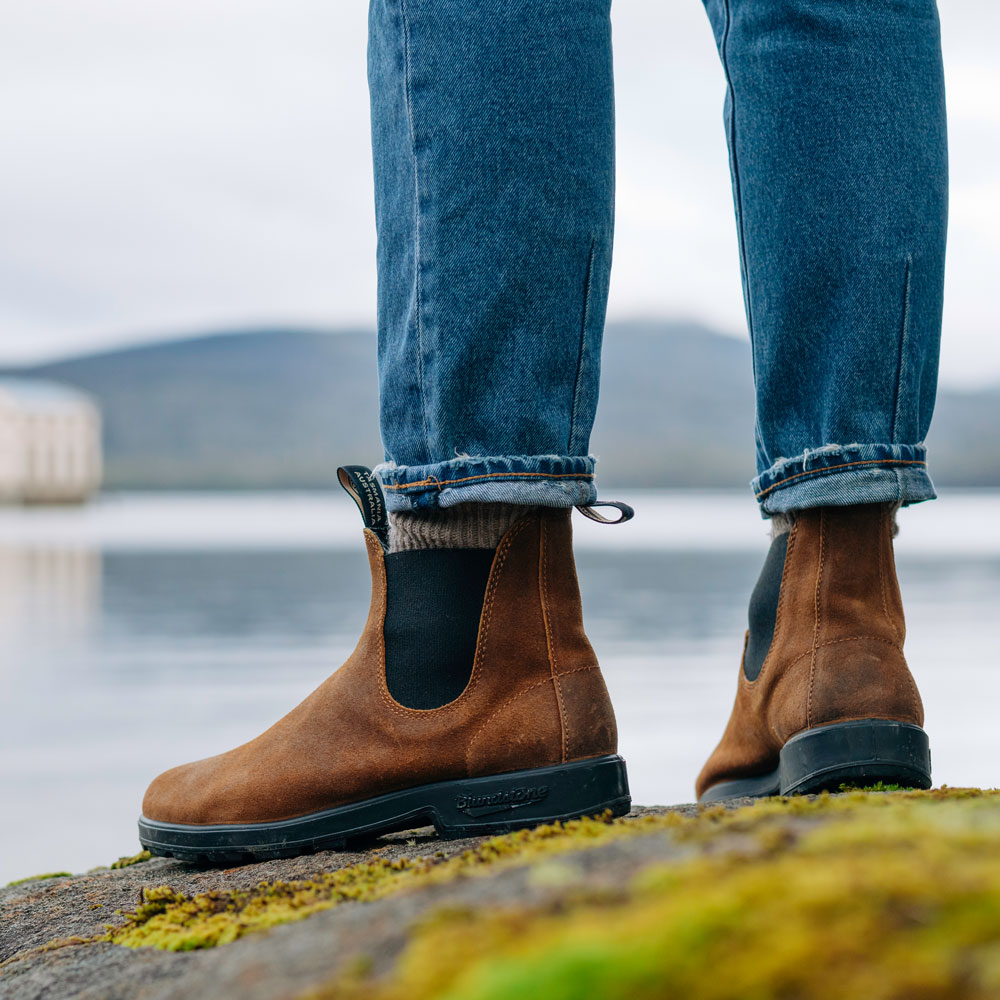 Braune Blundstone Chelsea Boots aus Veloursleder mit Jeans auf einem bemoosten Felsen am See